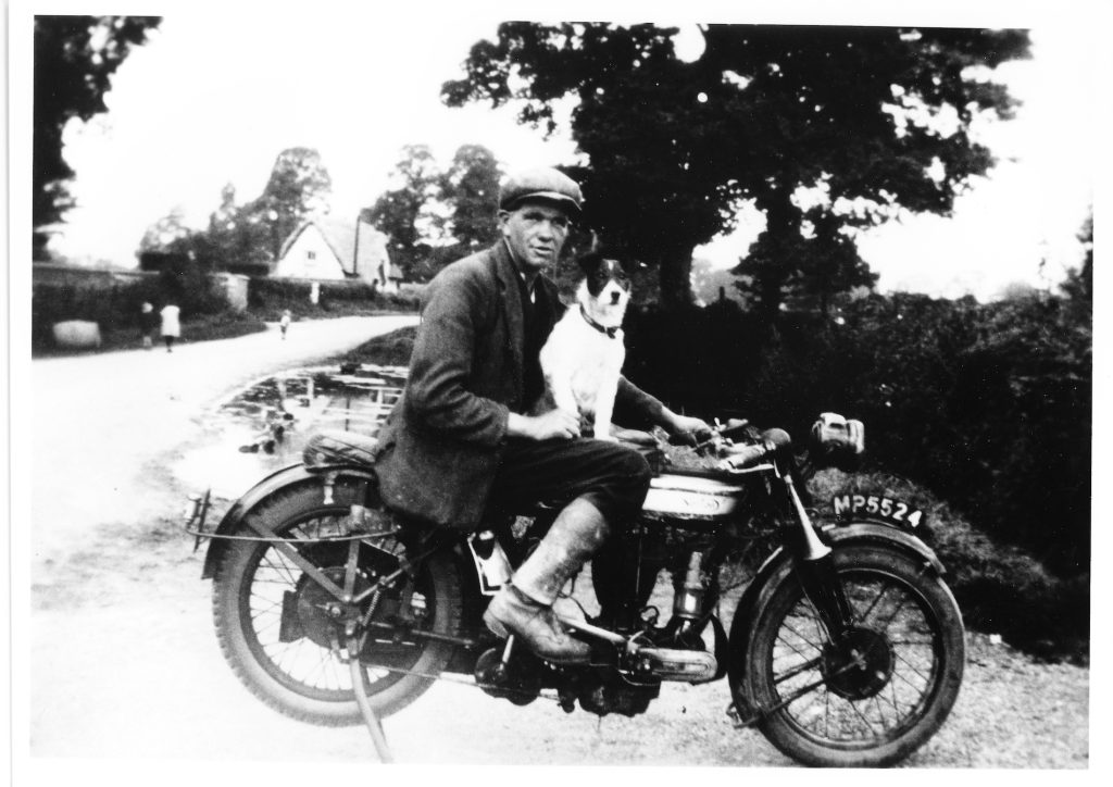 1930. Den Rumming on Norton motorcycle with his dog "Brandy", taken by the village pond. Manor Cottage on the left.